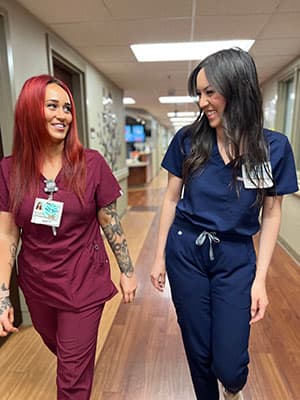 Two smiling nurses walking down a hallway in scrubs