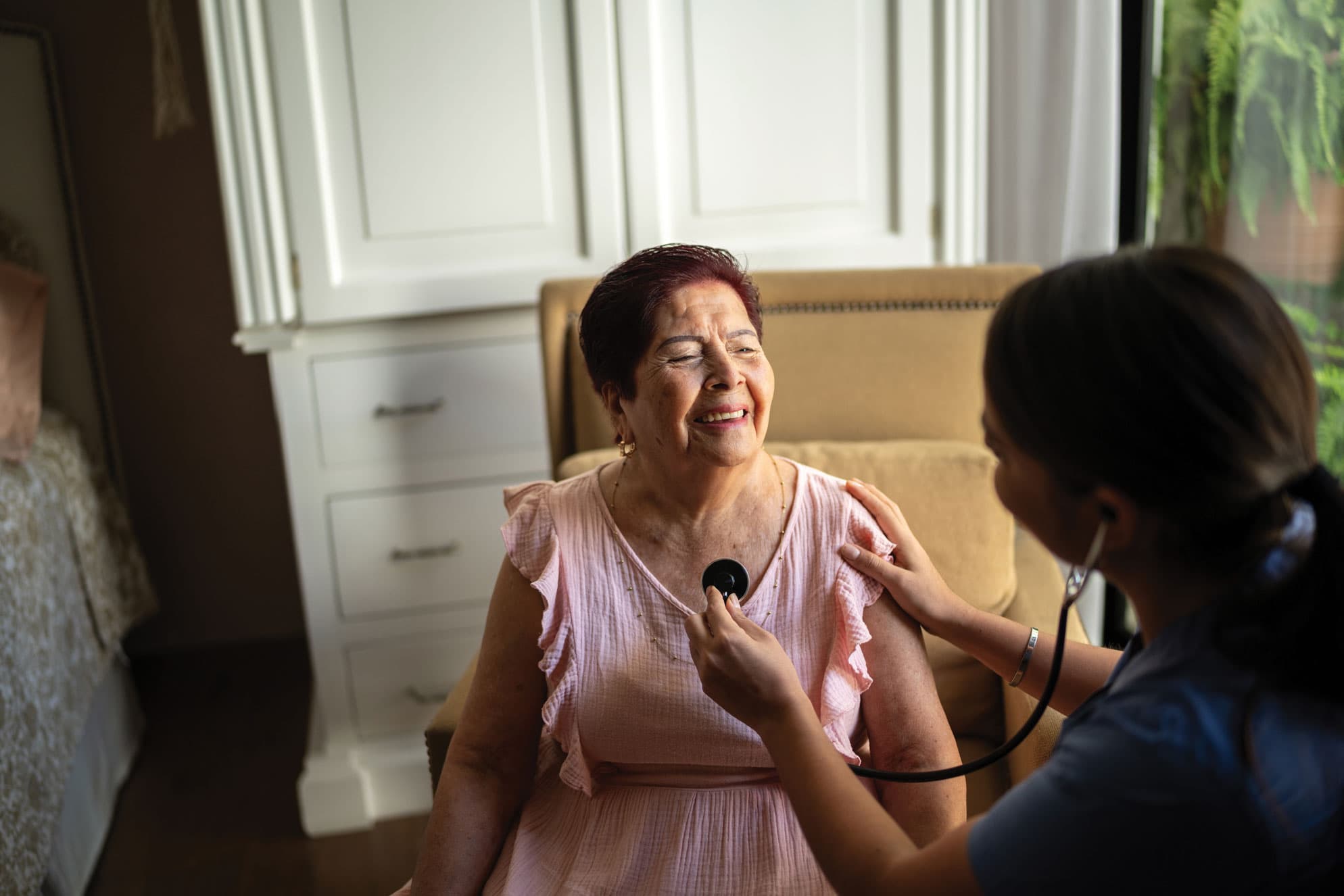 A nurse checking a pateint's heart with a stethoscope at her home